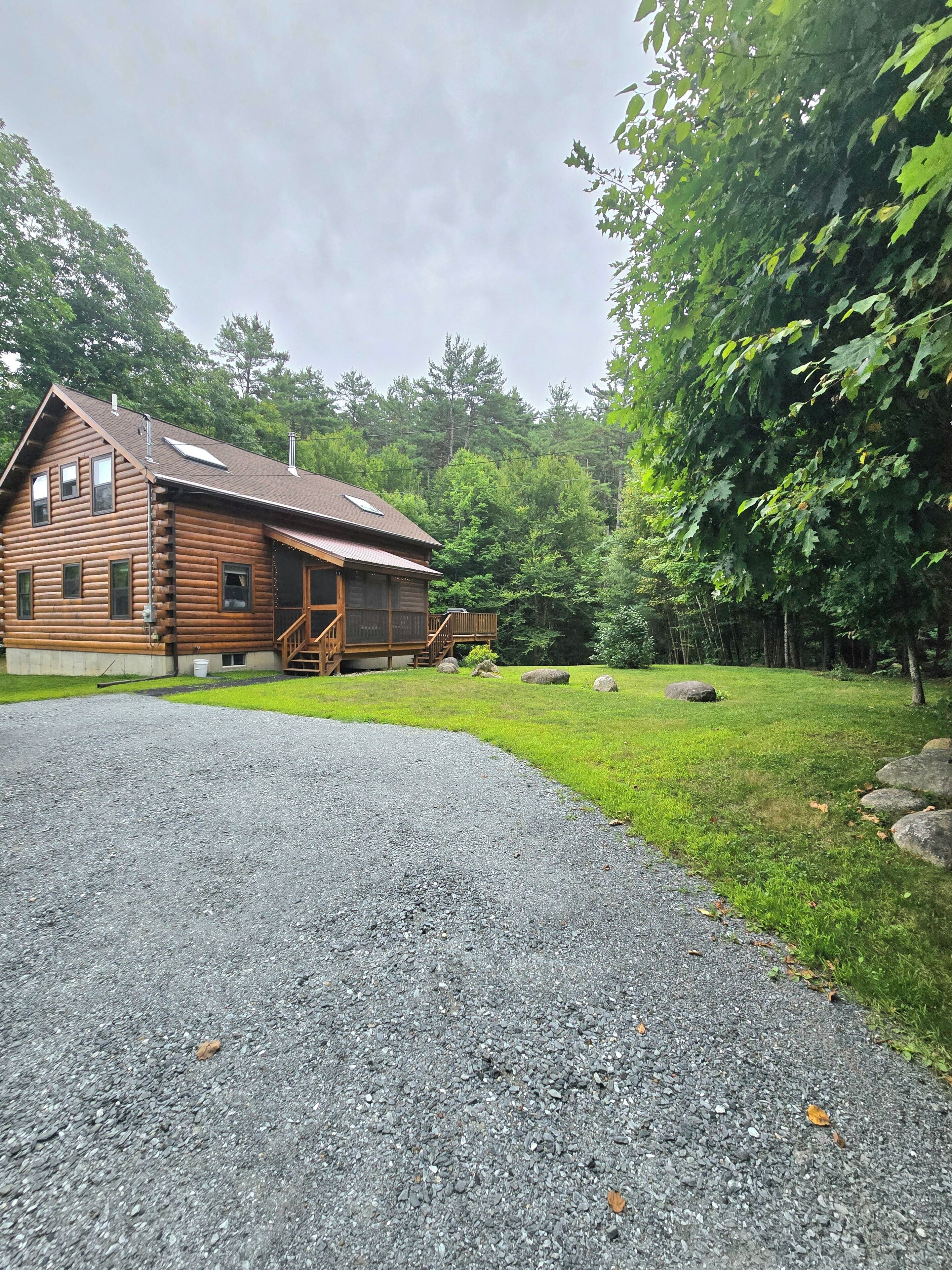 A log cabin with a gravel driveway and a grassy yard.