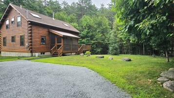 A log cabin with a gravel driveway and a grassy yard.