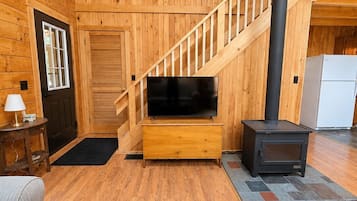Un interior de madera con una escalera, un televisor sobre un mueble de madera y una estufa negra.