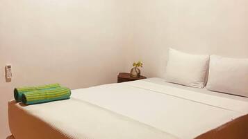 Habitación individual con techo de madera, una mesita de noche con un florero y una toalla verde sobre la cama.