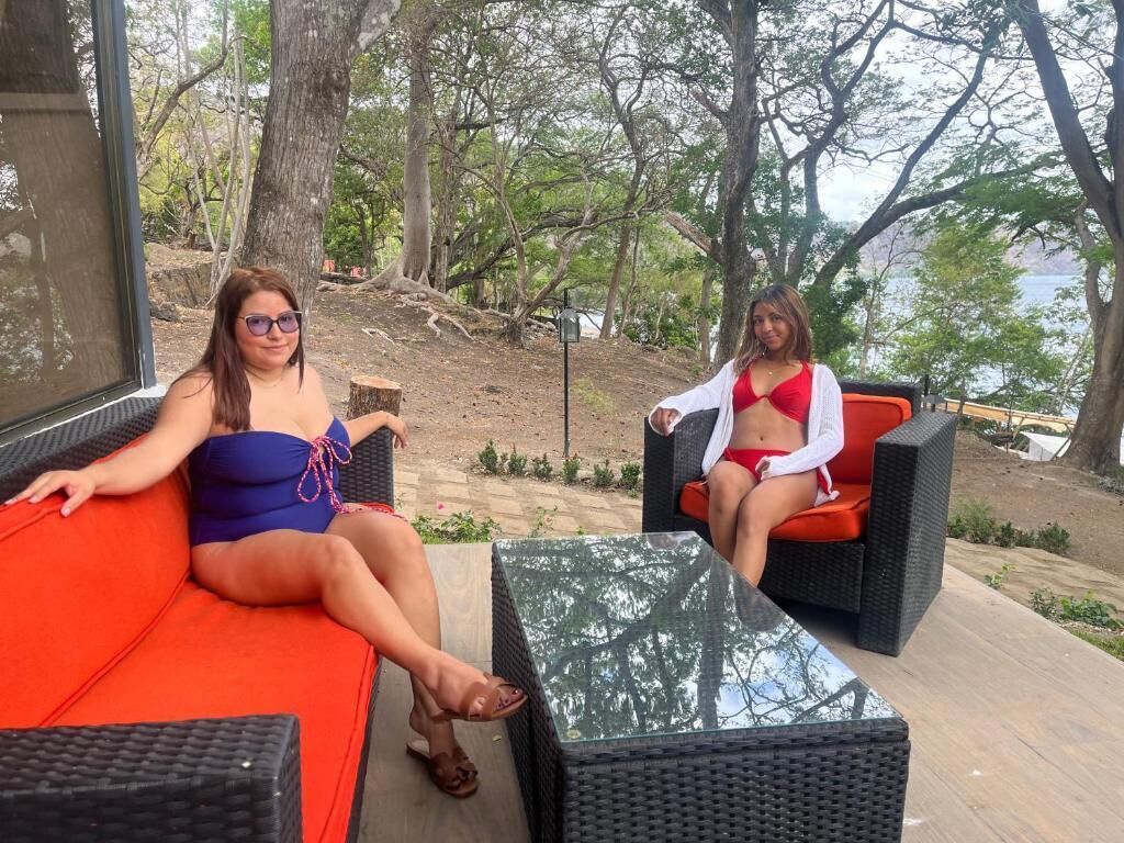 Two people sitting on outdoor furniture with a view of trees and a body of water.