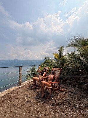 Two people sitting on wooden chairs by a poolside with a view of the sea and mountains in the background. - Casa Bambú Hotel (Catarina)