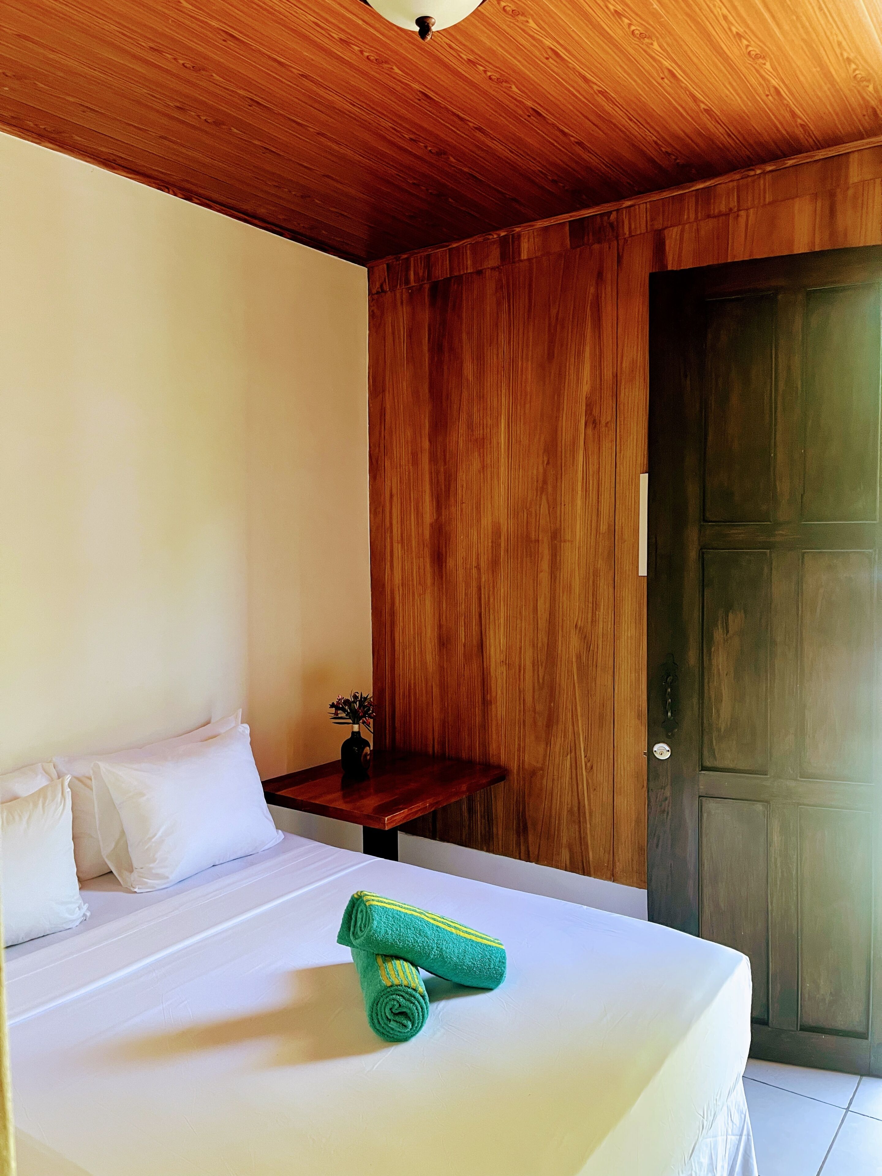 Una habitación con cama, una pequeña mesa de madera y una puerta.