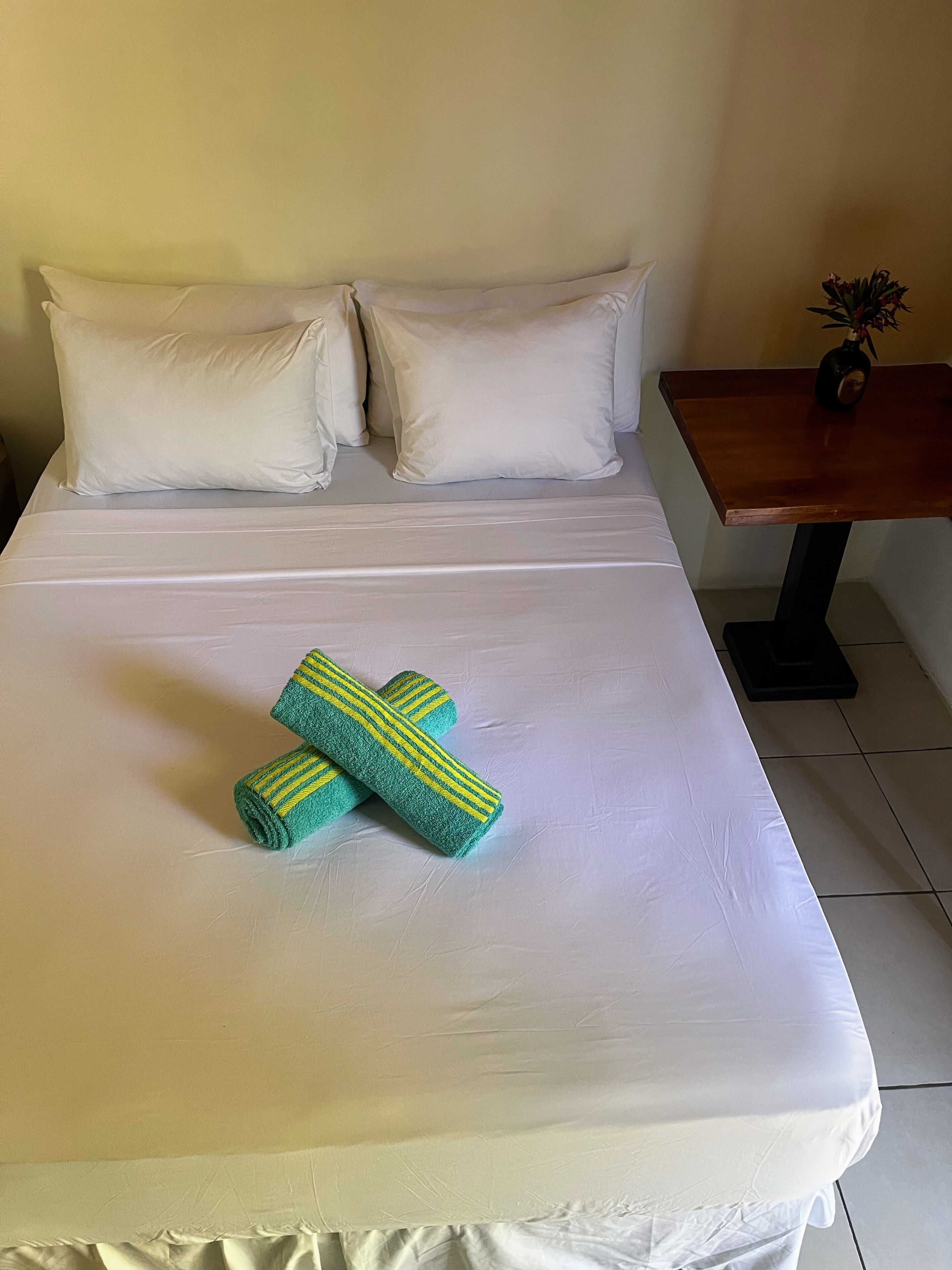 A neatly made bed with white linens and two rolled towels with green and yellow stripes.