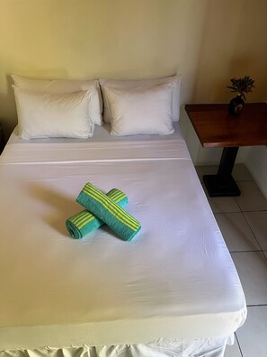 Een net opgemaakt bed met witte lakens en twee opgerolde handdoeken met groene en gele strepen.