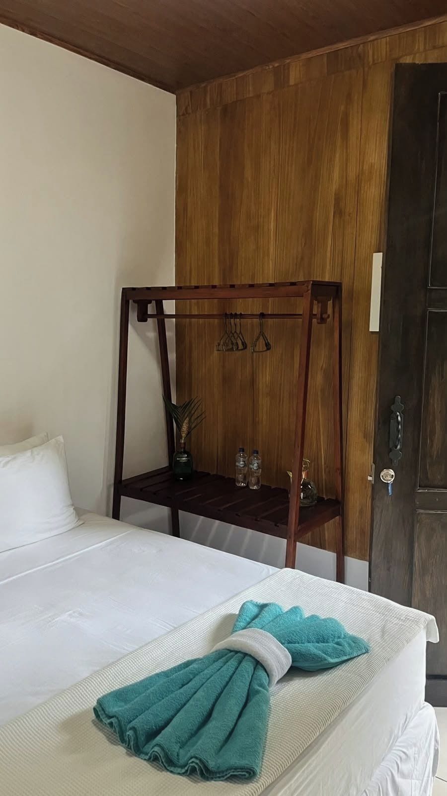 A hotel room with a bed, a wooden bench with hooks, and a door.