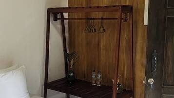 A hotel room with a bed, a wooden bench with hooks, and a door.