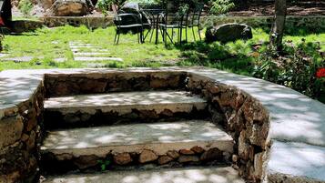 A set of stone steps leading to a seating area with metal chairs, surrounded by greenery and large rocks.