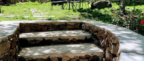 Un conjunto de escalones de piedra que conducen a un área de estar con sillas de metal, rodeada de follaje y grandes rocas.
