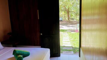 Quarto de hotel com cama, porta de madeira e vista para um jardim com caminho.