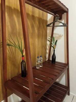 A wooden shelf unit with a slatted design, holding a potted plant, a bottle, and two water bottles.