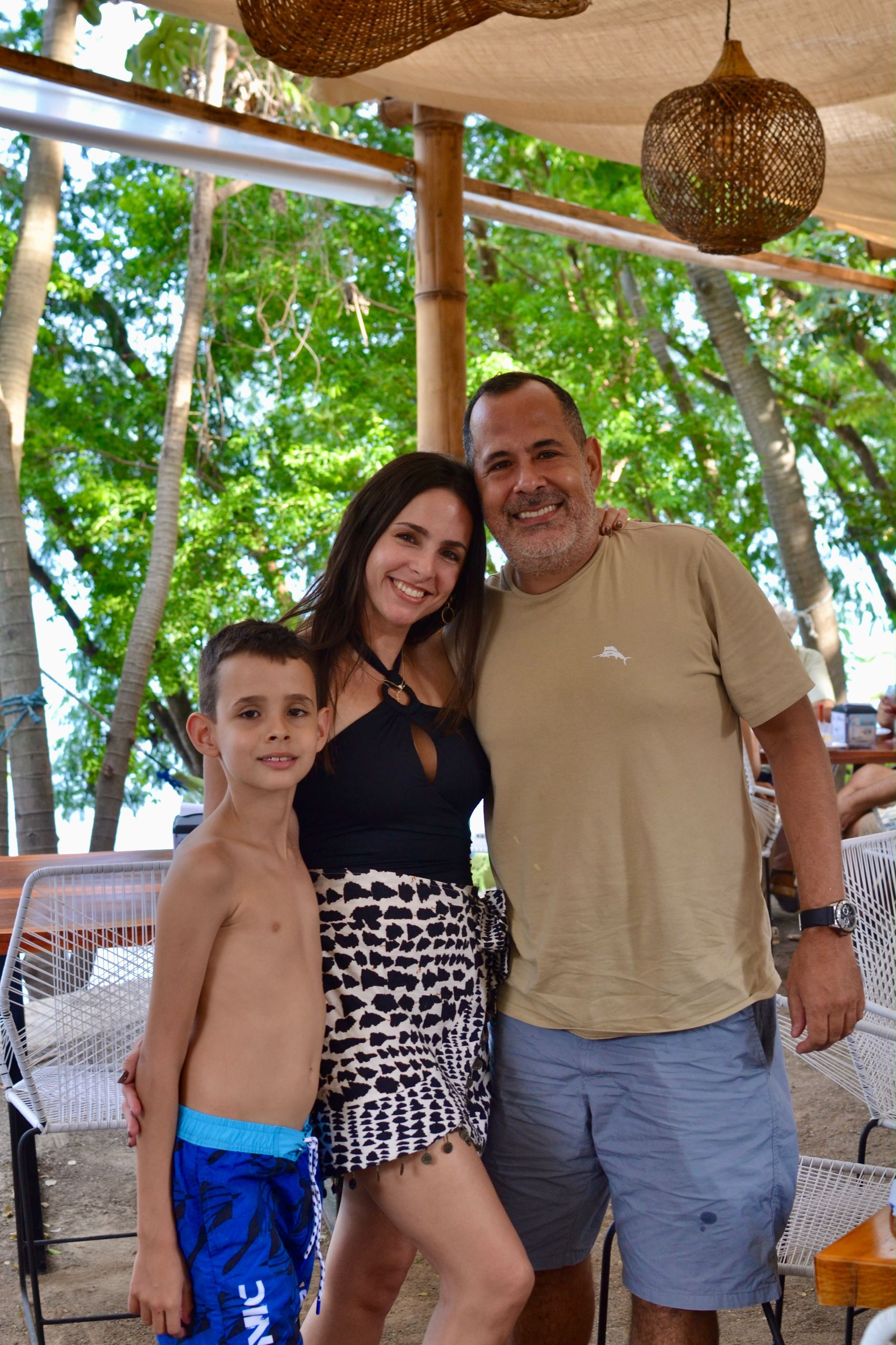 A family of three posing under a canopy with trees in the background.