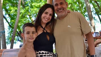A family of three posing under a canopy with trees in the background.