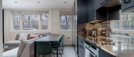 A modern kitchen with a built-in oven, a coffee machine, and a dining area with a bench and chairs.