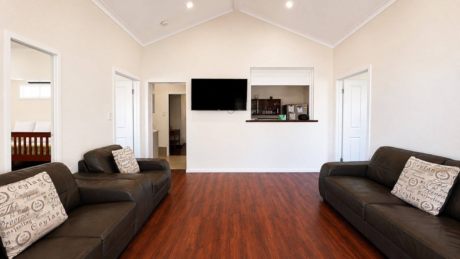 Un salon spacieux avec deux canapés en cuir, un téléviseur à écran plat fixé au mur et un plancher en bois.