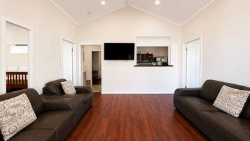 A spacious living room with two leather sofas, a flat-screen TV mounted on the wall, and a wooden floor.