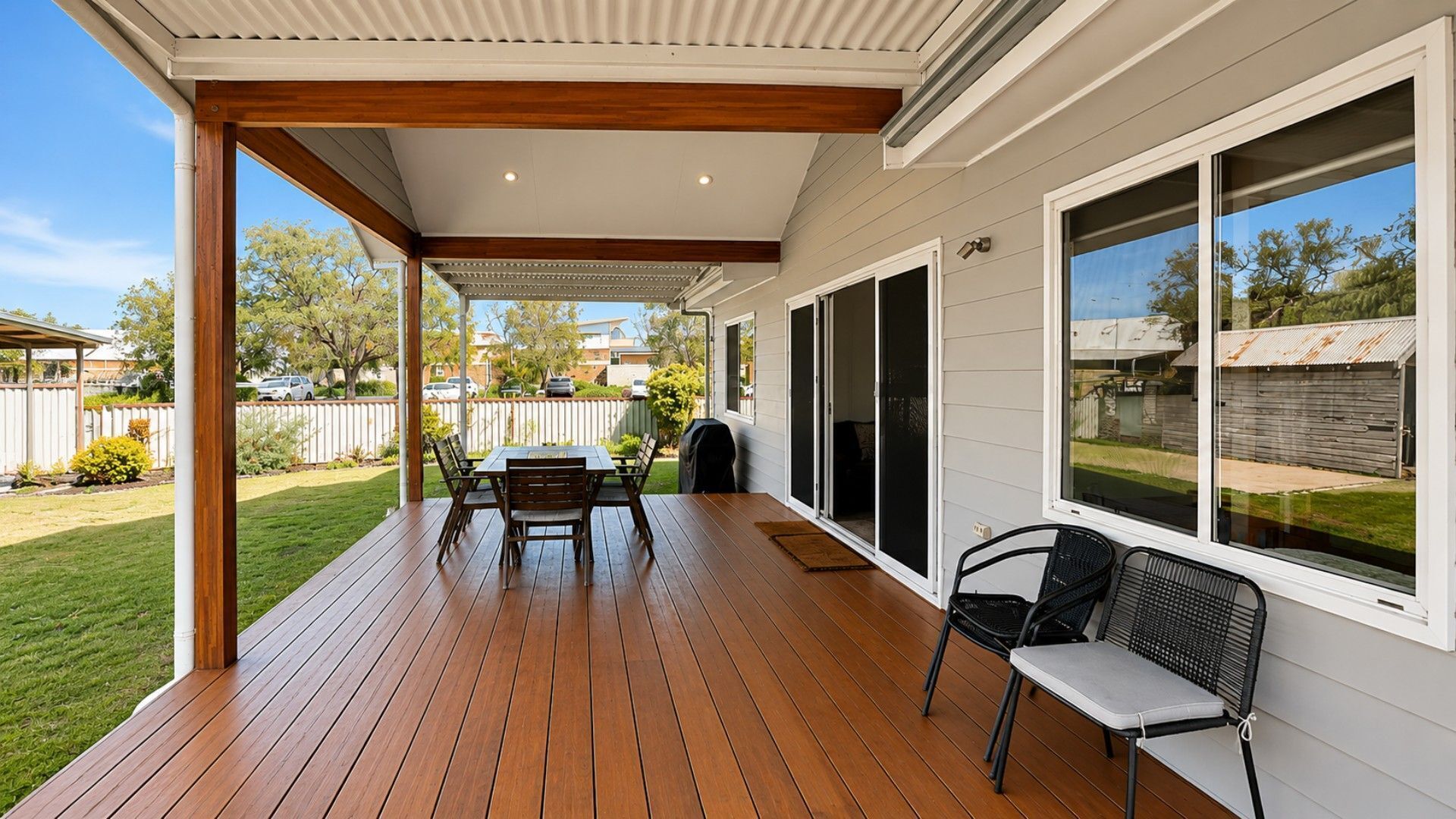 Eine überdachte Terrasse mit Holzdeck, einem Tisch mit Stühlen und Blick auf den Garten.