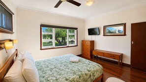 Un dormitorio con cama, cómoda, televisor y ventana con vista a árboles.