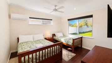 A bedroom with two beds, a ceiling fan, an air conditioning unit, and a window with a view of a backyard.