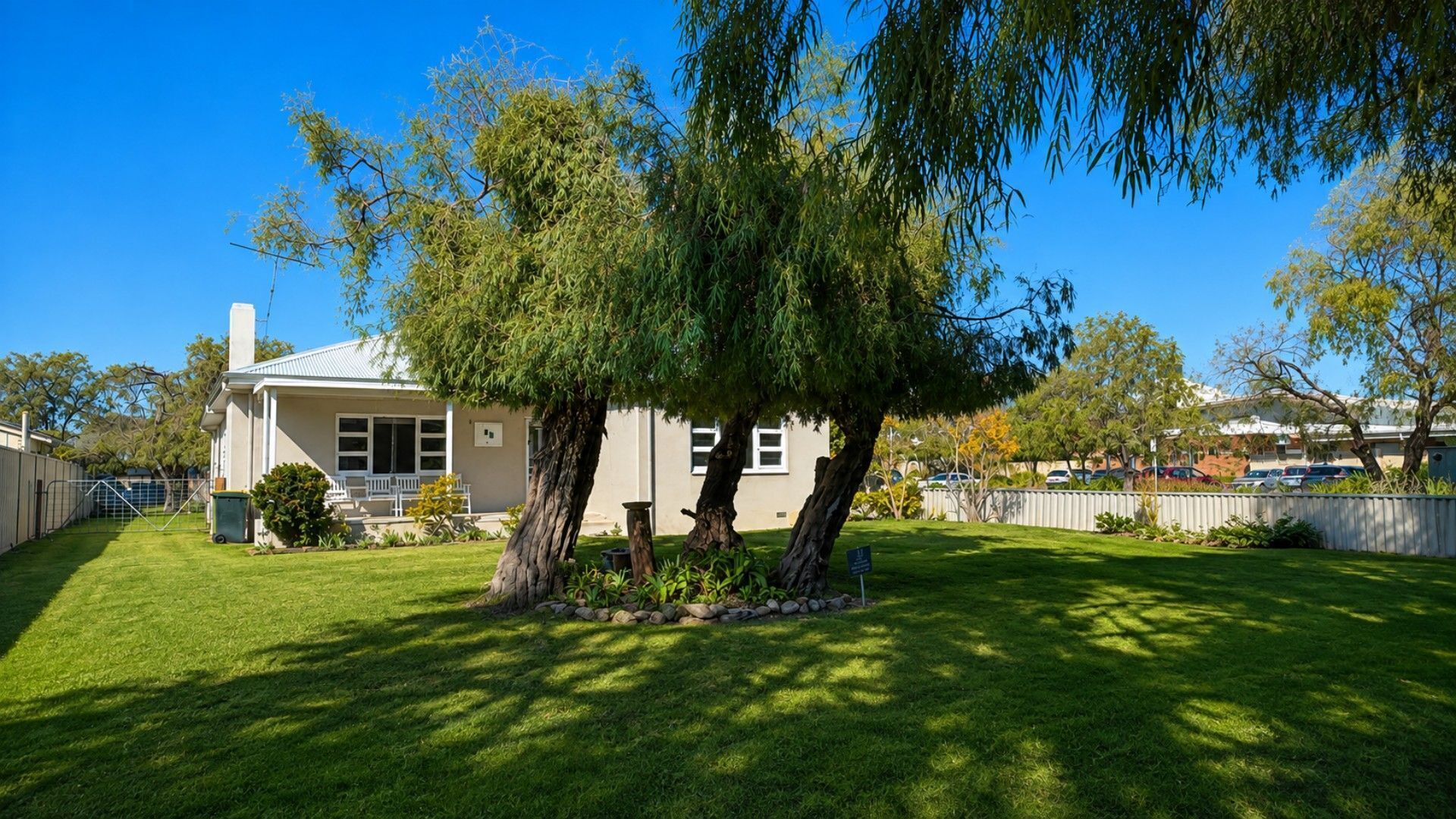 A residential property with a well-maintained lawn, a house with a white facade, and mature trees providing shade.