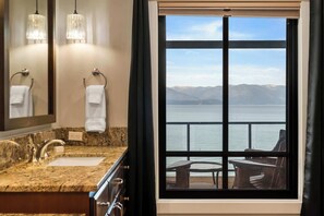 Baño con encimera de granito, dos lavamanos y un espejo grande. Dos toallas cuelgan de toalleros. Se ve una ventana con vistas a un lago y montañas.