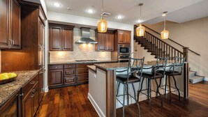 A kitchen with wooden cabinets, granite countertops, a stainless steel range hood, a built-in microwave, and a central island with bar stools. - Waterfront Townhouse, Private Hot Tub, Boat Slip (Sandpoint)