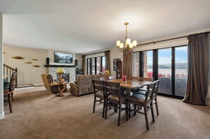 Una sala de estar amplia con chimenea, un comedor con candelabro y ventanas grandes que ofrecen vistas al exterior.