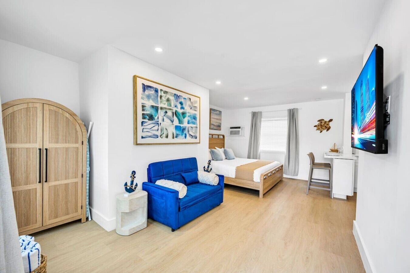 A modern bedroom with a bed, a blue sofa, a wooden wardrobe, a desk, and a flat-screen TV.