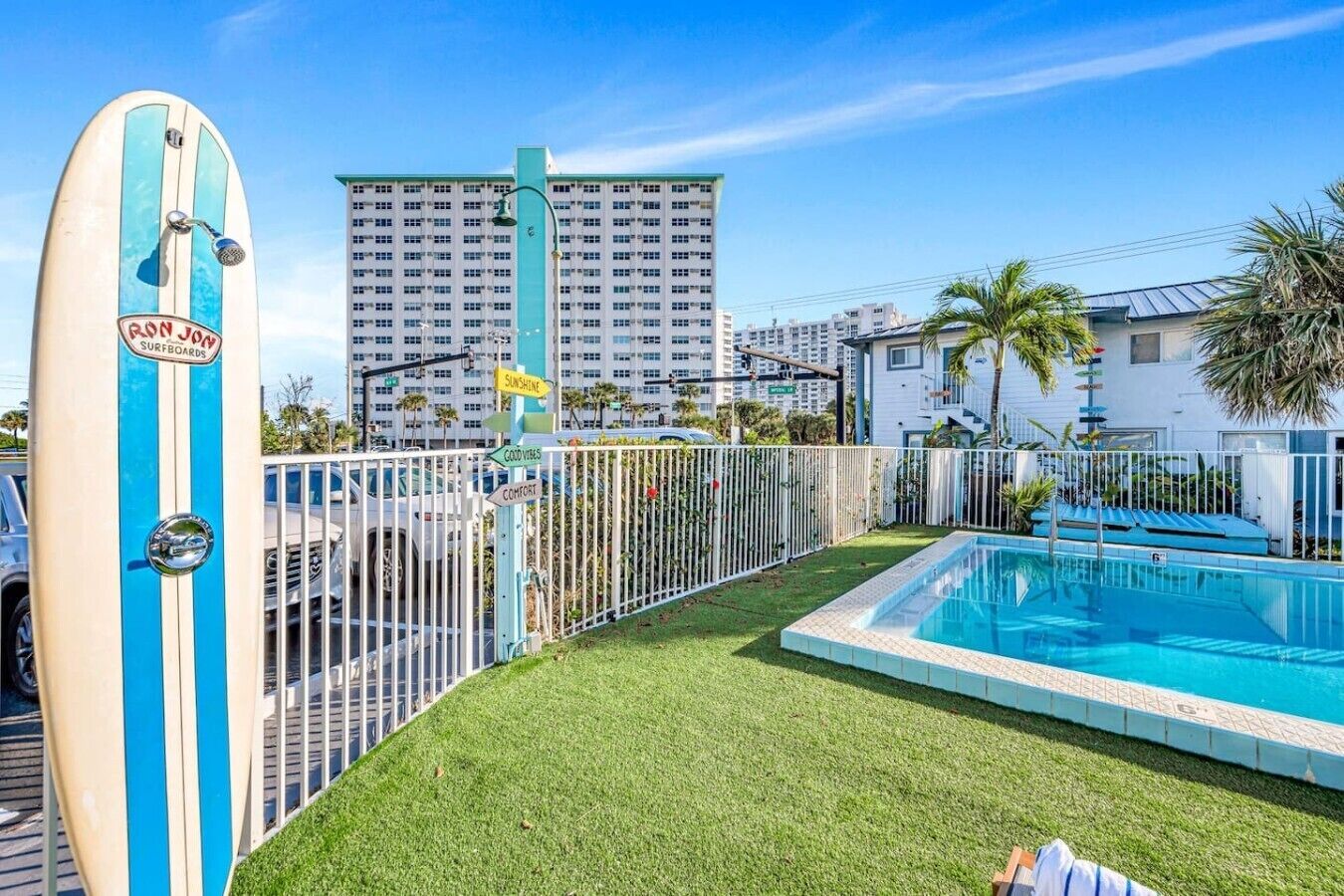 A swimming pool with a fenced area, a surfboard, and a tall building in the background.