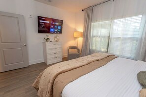 Een slaapkamer met een bed, een aan de muur bevestigde televisie, een lamp en een raam met gordijnen.