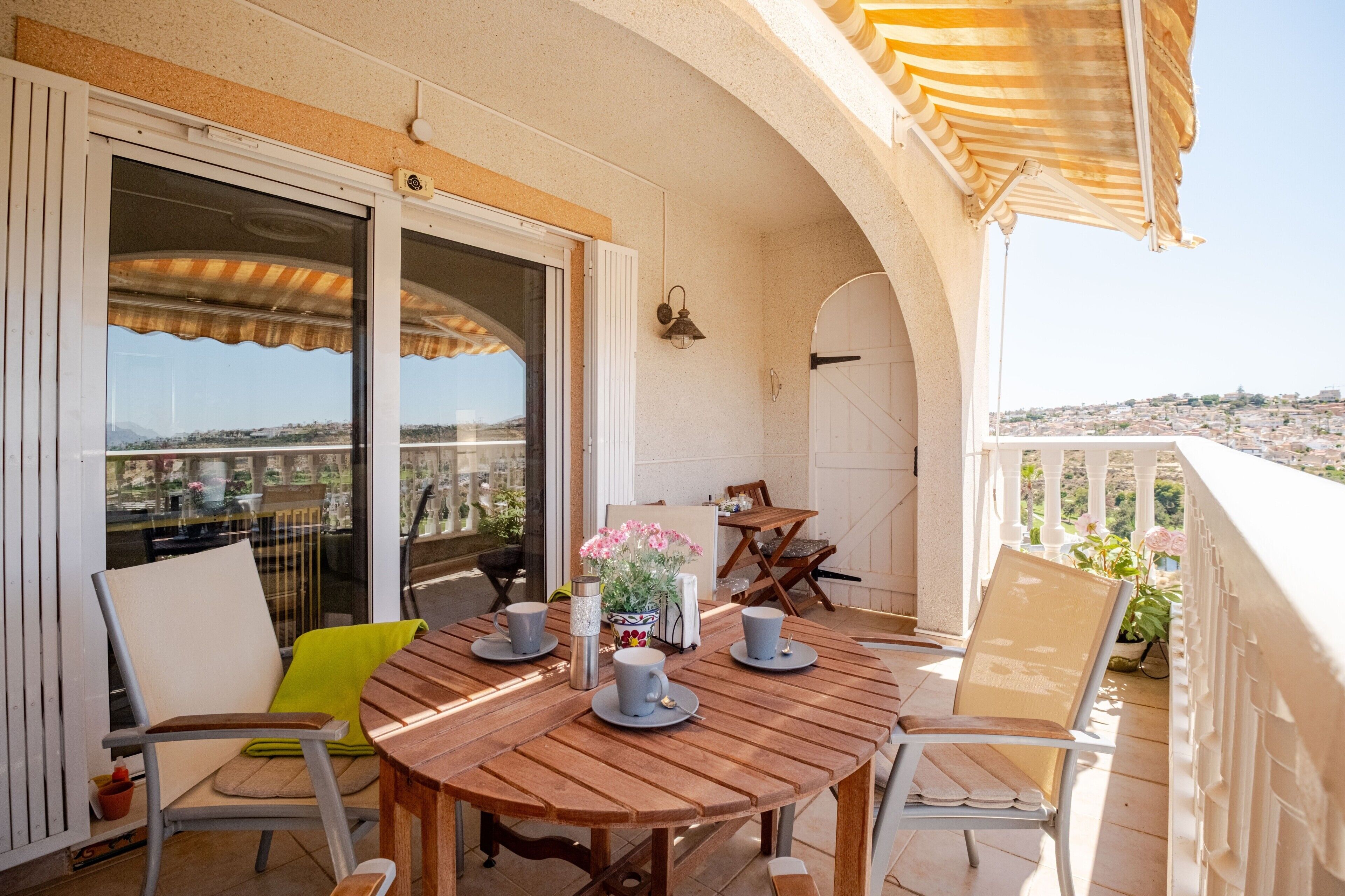 Une table en bois, entourée de chaises, sur un balcon offrant une vue sur le paysage urbain.