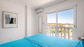 Une chambre avec une grande fenêtre, un ventilateur de plafond et un tableau accroché au mur.