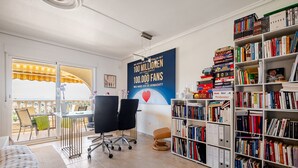 A room with a large bookshelf, a desk with chairs, and a poster on the wall.