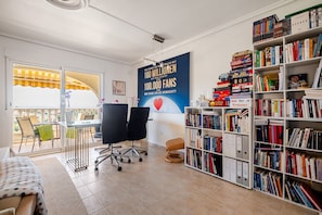A room with a large bookshelf, a desk with chairs, and a poster on the wall.