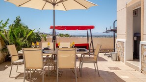 An outdoor patio with a table and chairs, a red canopy, and a view of the city and mountains.