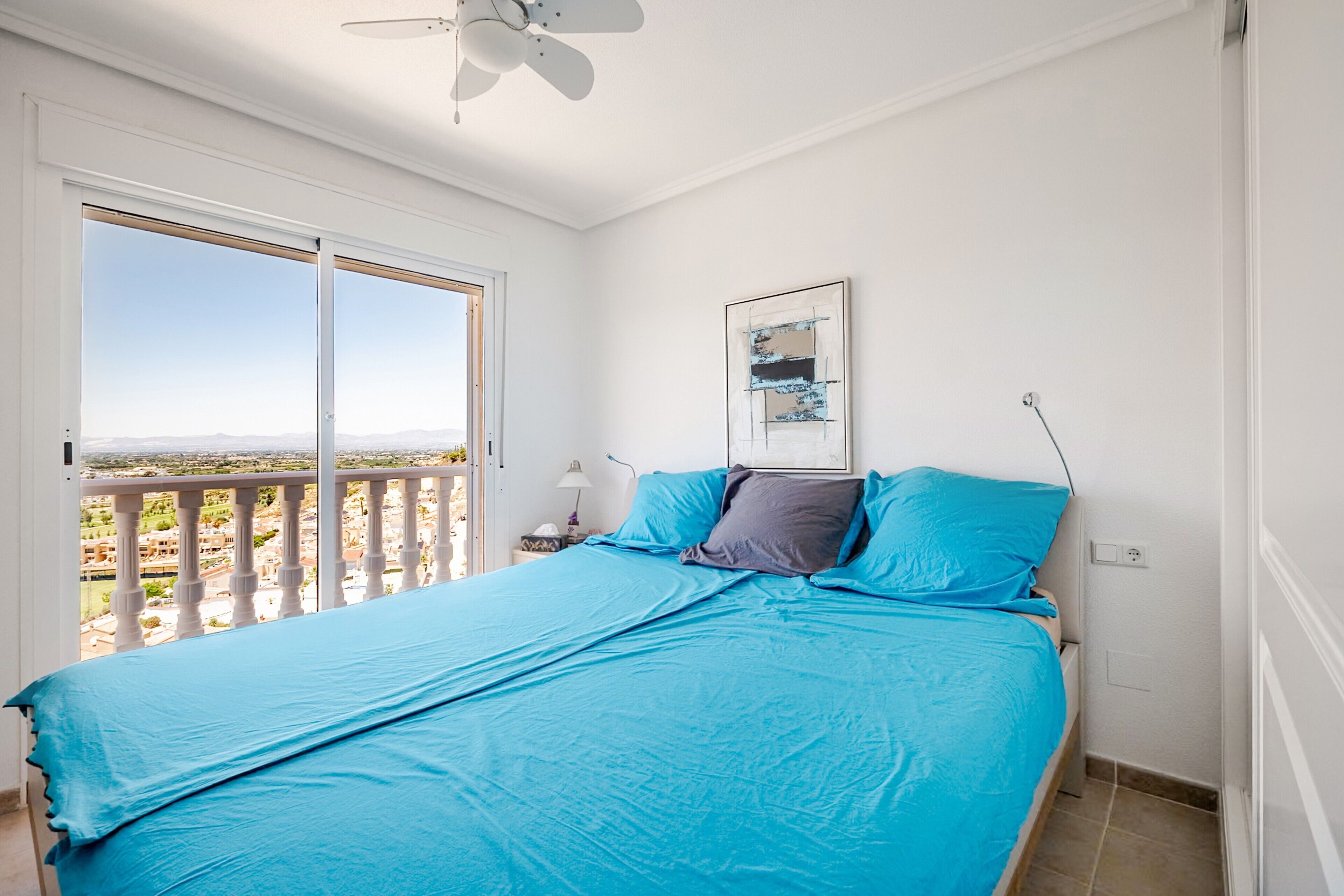 Une chambre avec un grand lit, un ventilateur de plafond, une fenêtre donnant sur un beau paysage et une table de chevet avec une lampe.