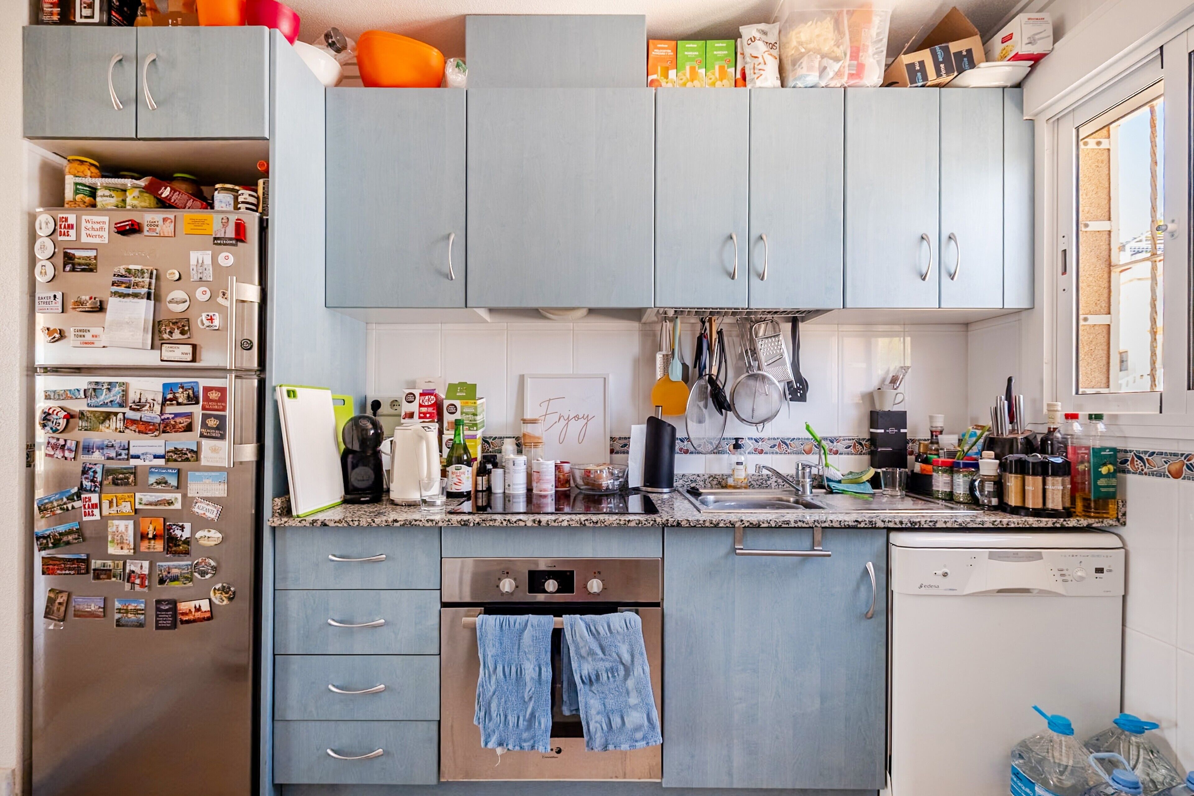 Una cocina con armarios grises, un refrigerador de acero inoxidable y varios utensilios de cocina sobre la encimera.