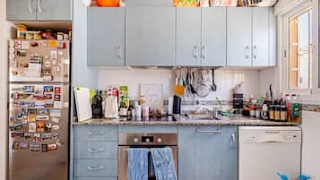 Una cocina con armarios grises, un refrigerador de acero inoxidable y varios utensilios de cocina sobre la encimera.