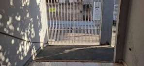 A gated entrance with a metal fence, a concrete pathway leading to a building, and a sign on the wall.