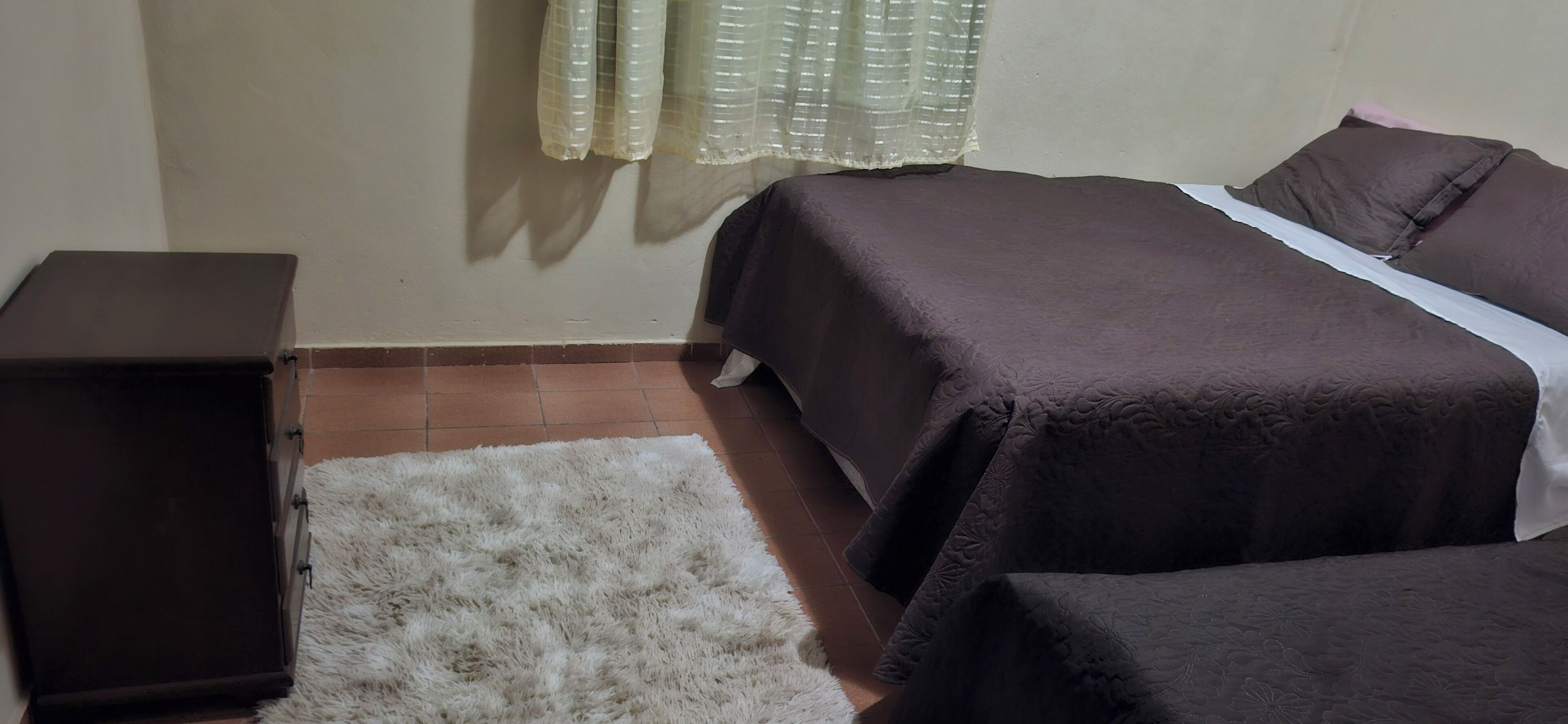 Un dormitorio con una cama, una mesita de noche pequeña y una alfombra blanca.