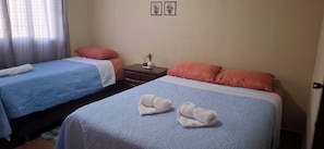 A hotel room with two beds, each with a blue and white bedspread, and a nightstand with a vase and a small plant.