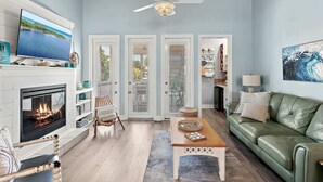 A living room with a fireplace, a television, a ceiling fan, and a green couch. - Steps to the Private Beach, renovated, 3 Bikes - Time to Coast (Santa Rosa Beach)