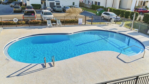 A swimming pool with a clear blue water, surrounded by a fence, and adjacent to a parking area with several cars. - Steps to the Private Beach, renovated, 3 Bikes - Time to Coast (Santa Rosa Beach)