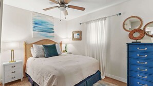 A bedroom with a bed, bedside tables, a dresser, a ceiling fan, a painting, and a mirror. - Steps to the Private Beach, renovated, 3 Bikes - Time to Coast (Santa Rosa Beach)