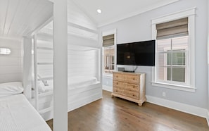 Ein Schlafzimmer mit Etagenbett, Kommode, Flachbildfernseher und einem Fenster mit Jalousien.