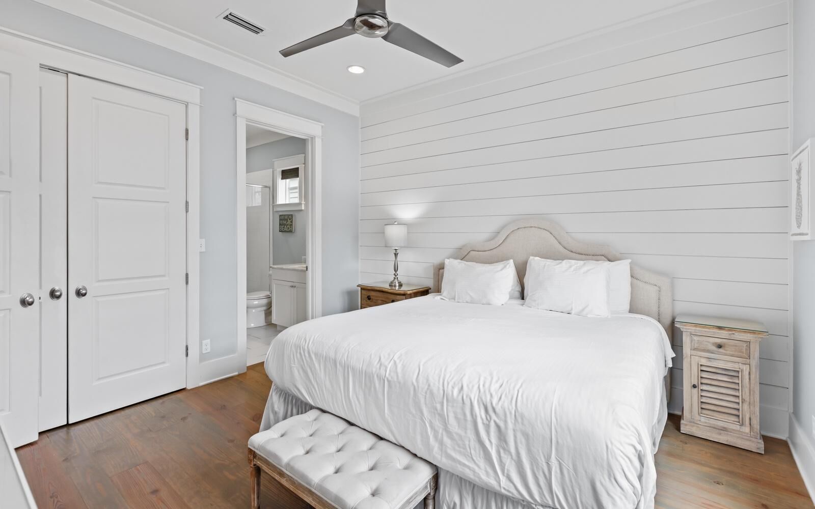 Una camera da letto con un letto, una panca, un comodino, una ventola a soffitto e una porta.
