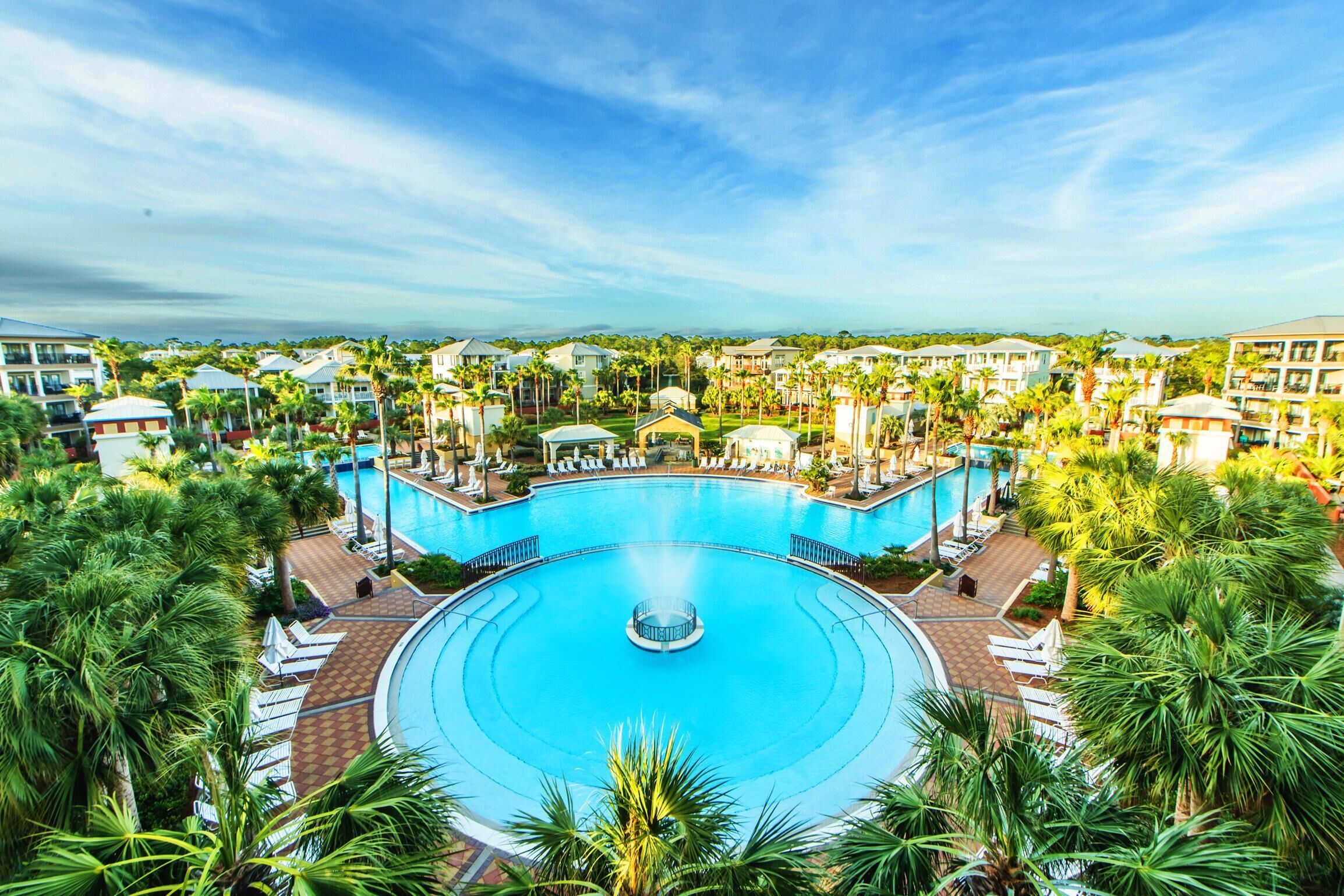 A large circular pool with a central fountain, surrounded by lounge chairs and palm trees.