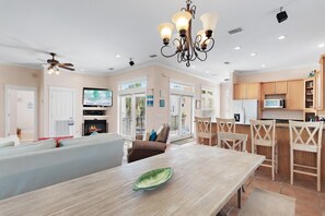 A spacious living area with a fireplace, a dining table, and a kitchen area with wooden cabinets. - The Mermaid (Panama City Beach)