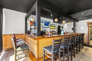 A bar area with a wooden counter, multiple bar stools, and hanging pendant lights. - Tidewater 2112 (Panama City Beach)