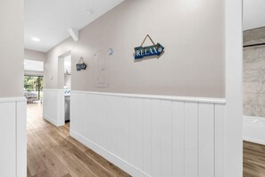 Un pasillo con paneles blancos, suelo de madera y vista a una habitación con un gran ventanal.